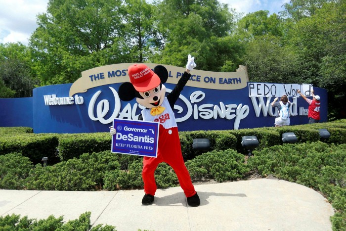 A person wearing a mouse costume dances while holding a poster of Florida governor Ron DeSantis outside Walt Disney World in Orlando