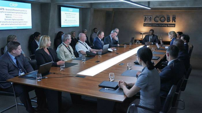 A man sits at the end of a long conference table filled with people